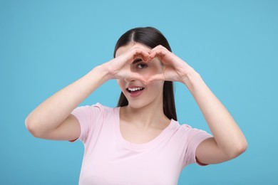 Beautiful young woman making heart with hands on light blue background