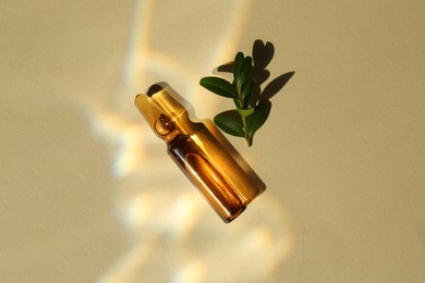 Skincare ampoule and leaves in sunlight on beige background, top view