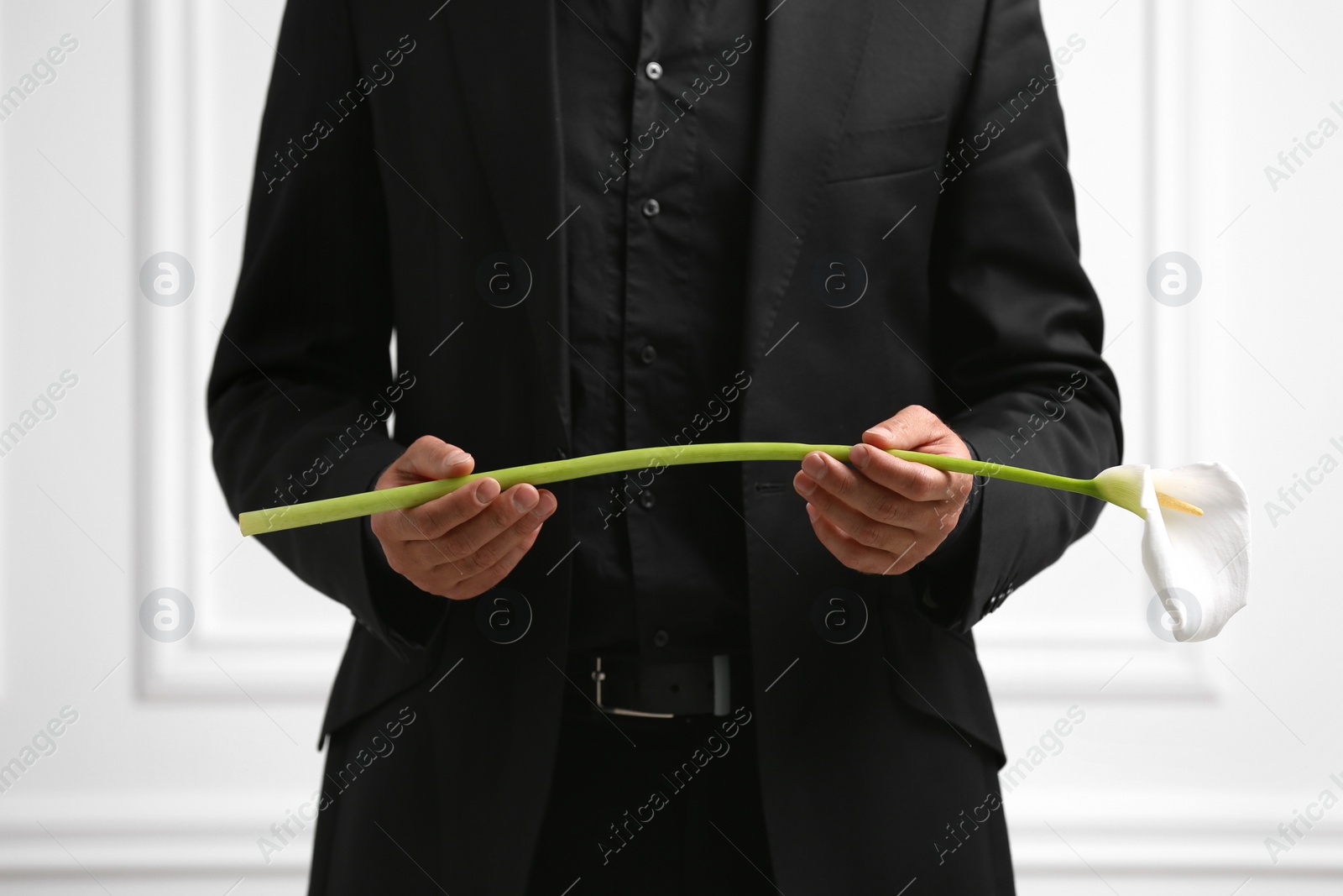 Photo of Man with calla lily flower near white wall, closeup. Funeral ceremony