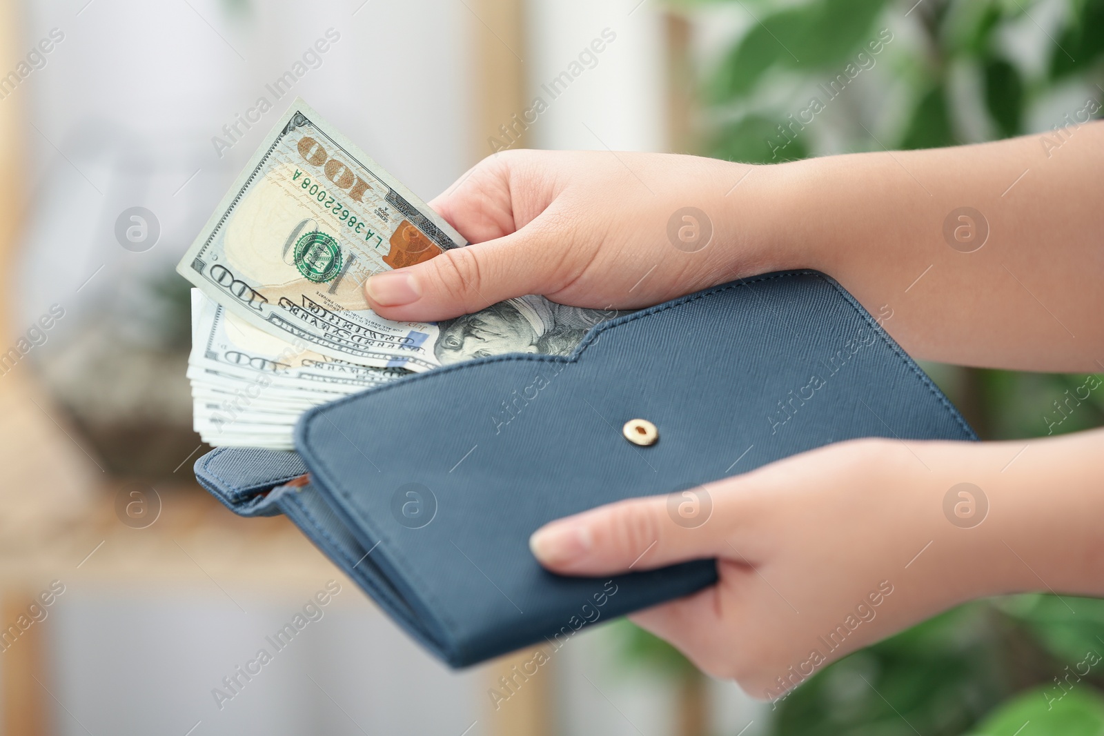 Photo of Woman putting money into wallet on blurred background, closeup