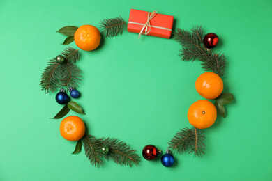 Frame made of ripe tangerines, fir branches and Christmas decor on green background, flat lay with space for text