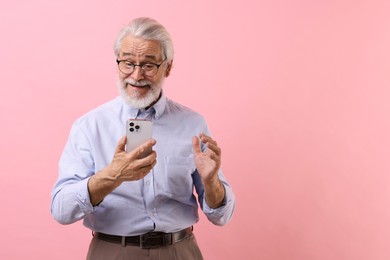 Photo of Portrait of stylish grandpa with glasses using smartphone on pink background, space for text