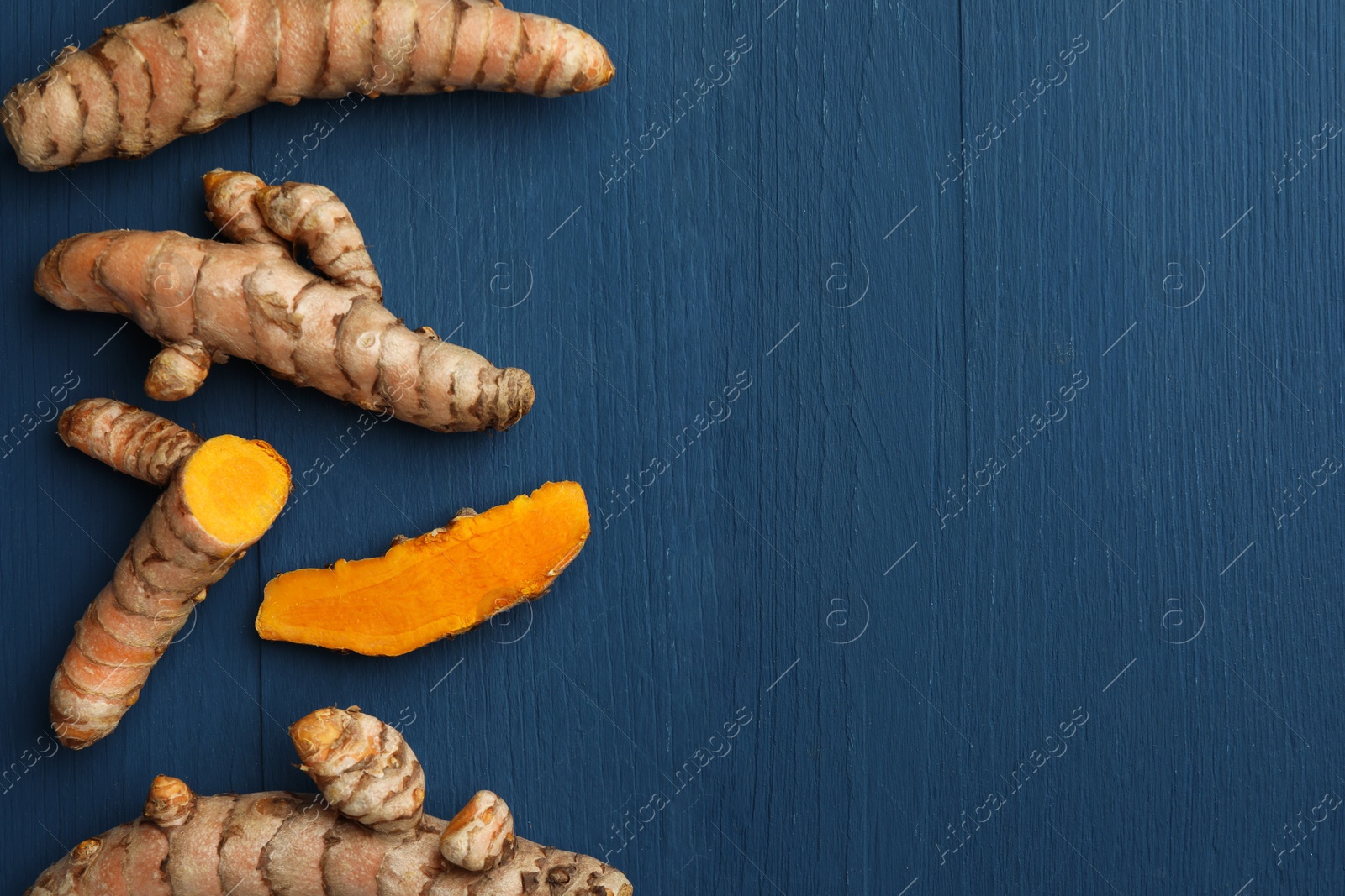 Photo of Whole and cut turmeric roots on blue wooden table, flat lay. Space for text