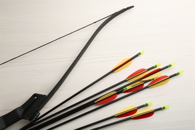 Photo of Plastic arrows and bow on white wooden table, flat lay. Archery sports equipment