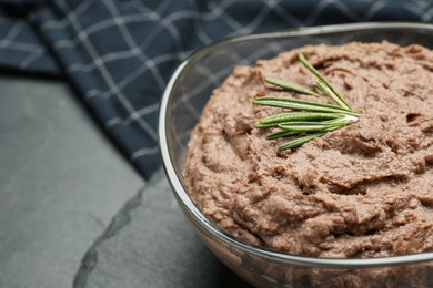 Photo of Tasty liver pate with rosemary in glass bowl on black table, closeup. Space for text