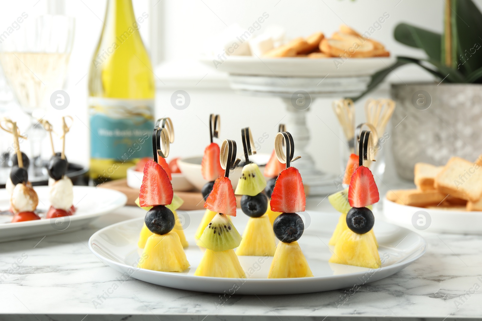 Photo of Tasty canapes with pineapple, kiwi and berries on white marble table, closeup