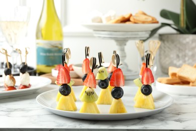 Tasty canapes with pineapple, kiwi and berries on white marble table, closeup