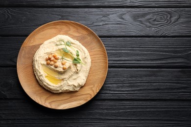 Photo of Bowl of tasty hummus with chickpeas on black wooden table, top view. Space for text