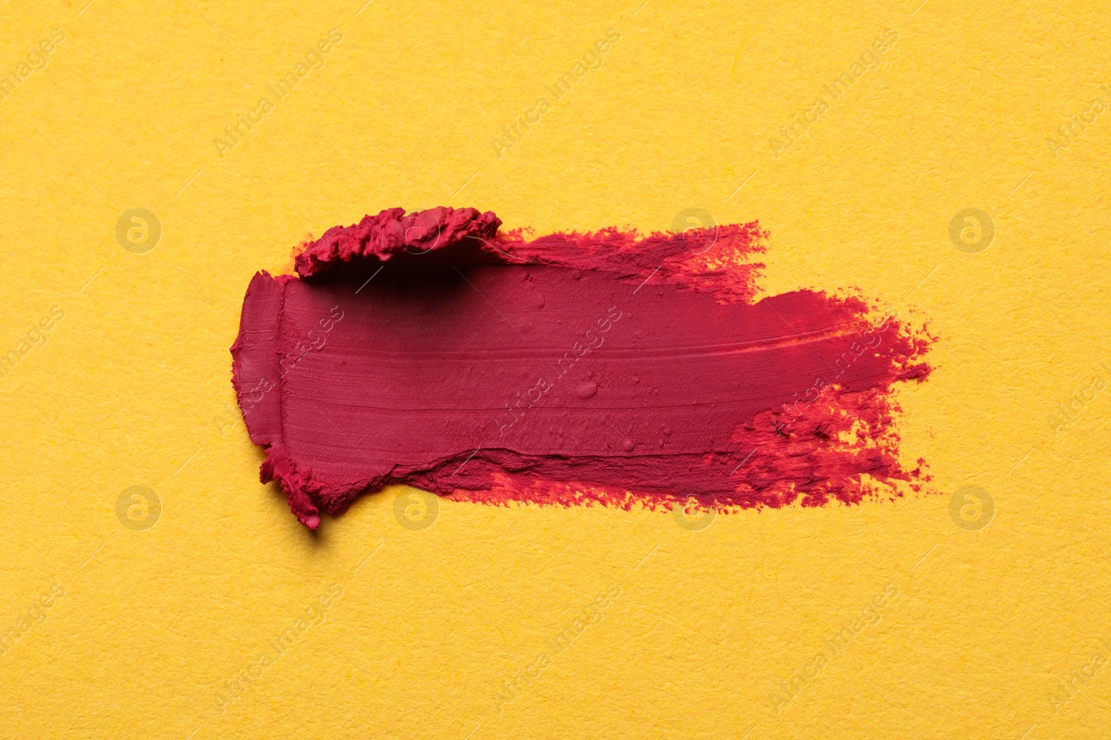 Photo of Smear of bright lipstick on yellow background, top view