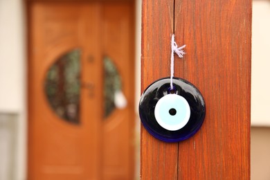 Photo of Evil eye amulet hanging on wooden pillar outdoors, closeup. Space for text