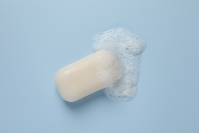 Photo of Soap with fluffy foam on light blue background, top view