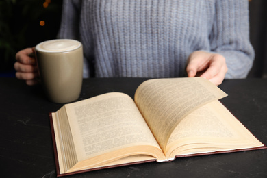 Woman with cup of coffee reading book at table, closeup