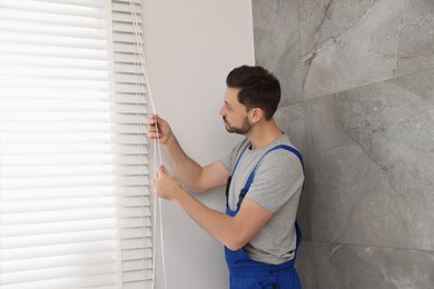 Photo of Worker in uniform opening or closing horizontal window blind indoors