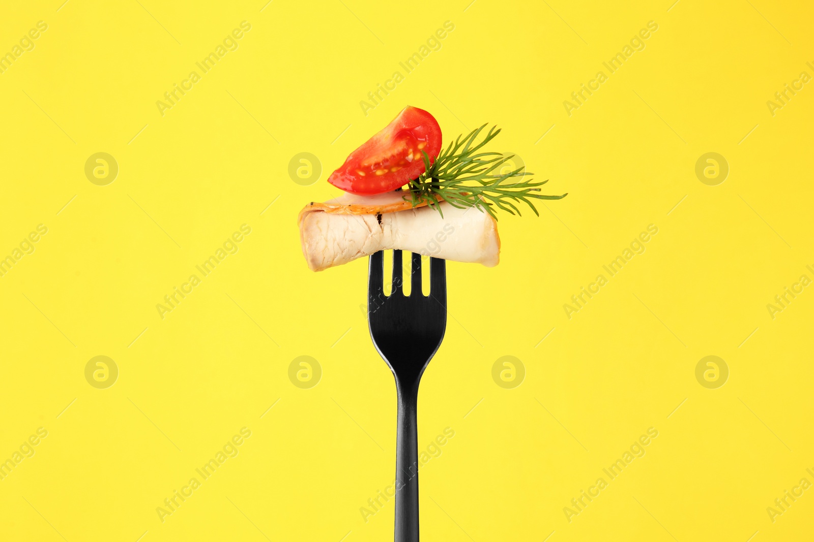 Photo of Fork with slice of ham, cut tomato and dill on yellow background