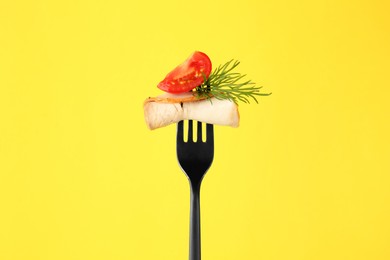 Fork with slice of ham, cut tomato and dill on yellow background