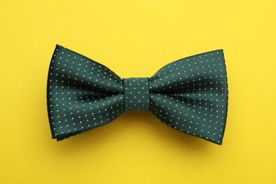 Stylish green bow tie with polka dot pattern on yellow background, top view