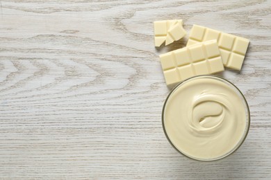 Photo of Tasty white chocolate paste in bowl and pieces on light wooden table, top view. Space for text