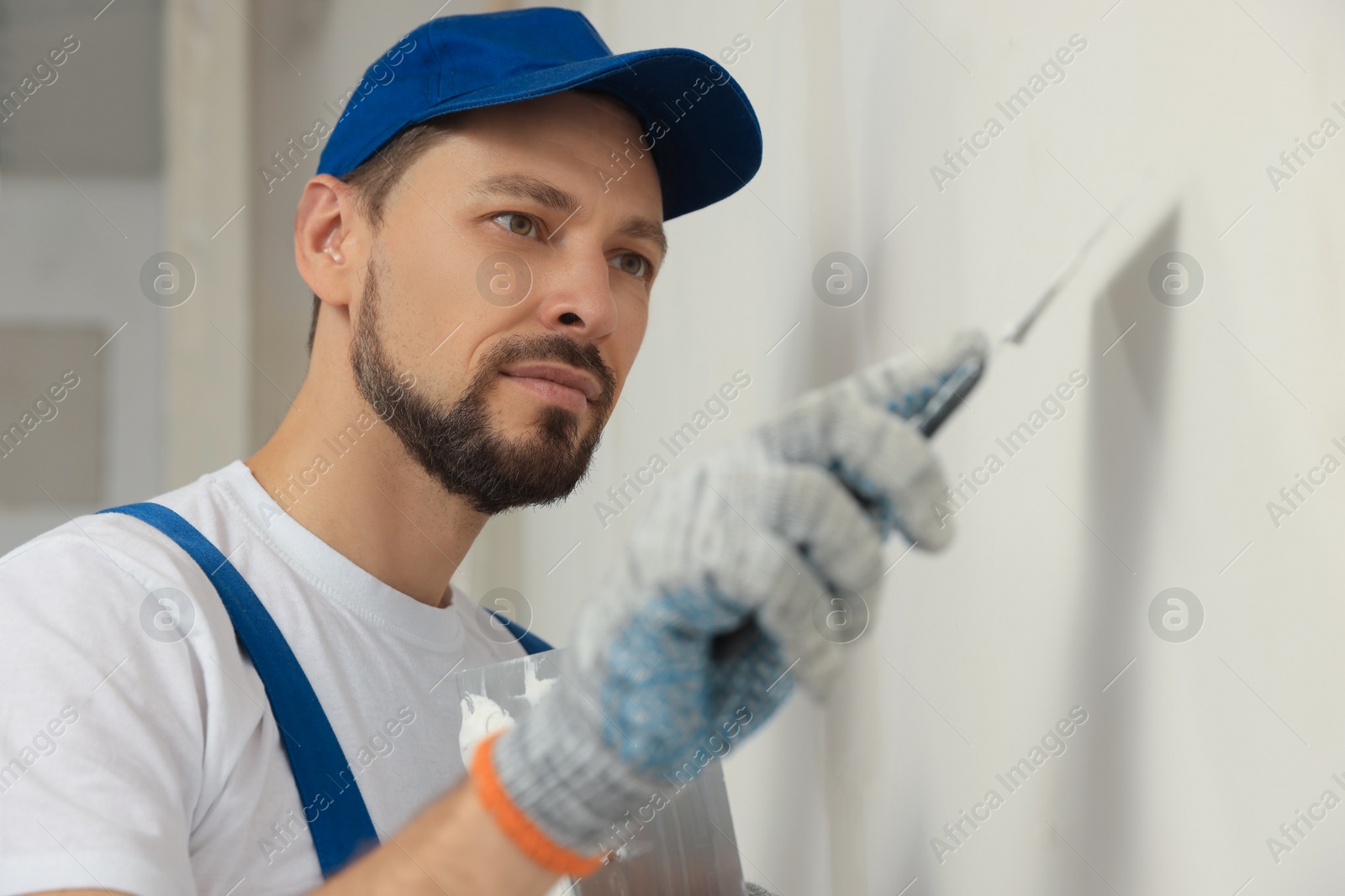 Photo of Professional worker plastering wall with putty knife indoors