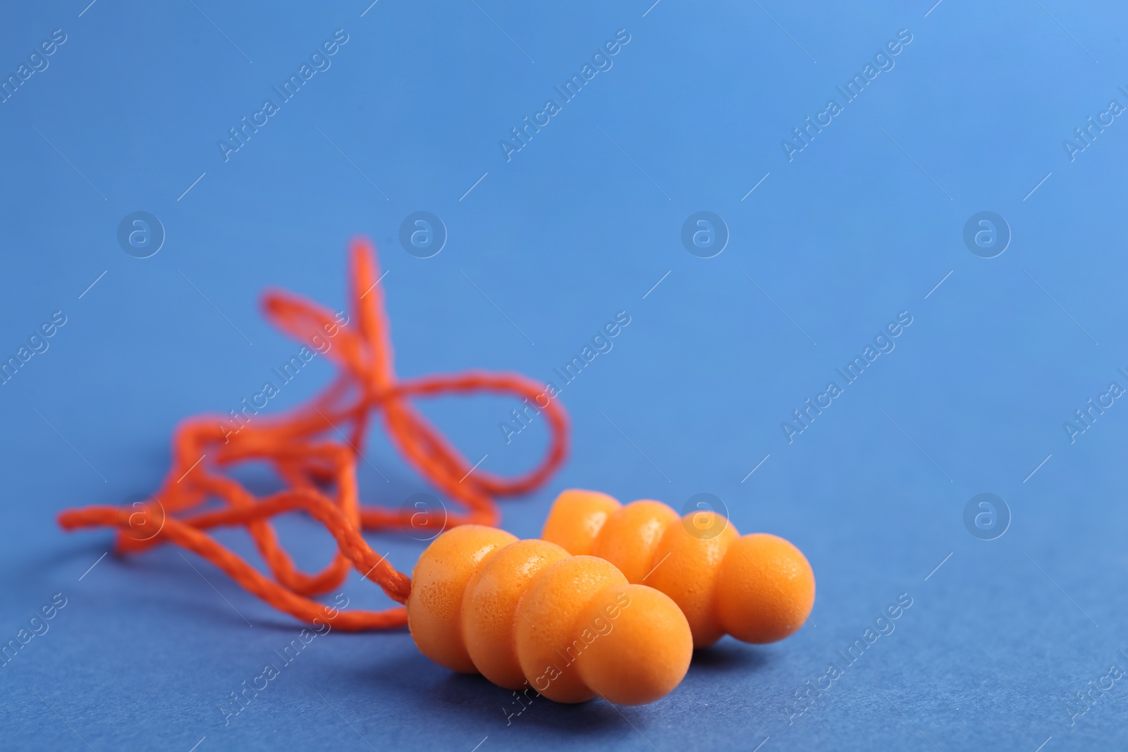 Photo of Pair of orange ear plugs with cord on blue background, closeup. Space for text