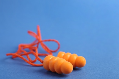Pair of orange ear plugs with cord on blue background, closeup. Space for text