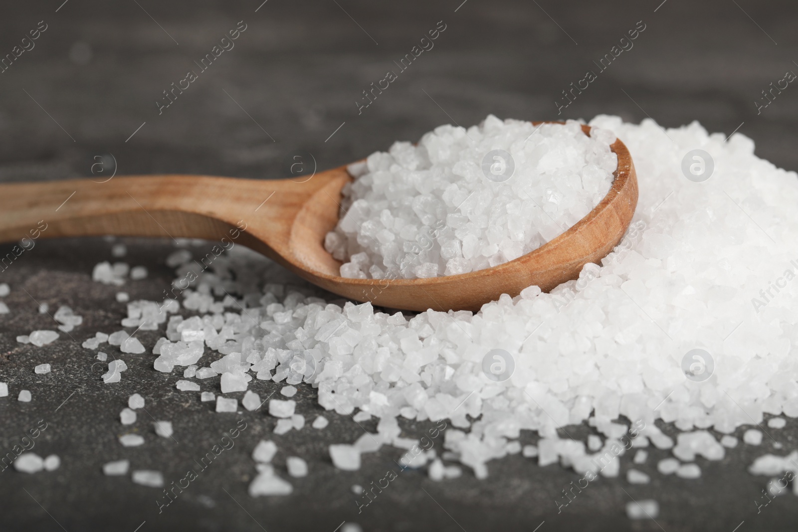 Photo of Natural sea salt and wooden spoon on grey table, closeup