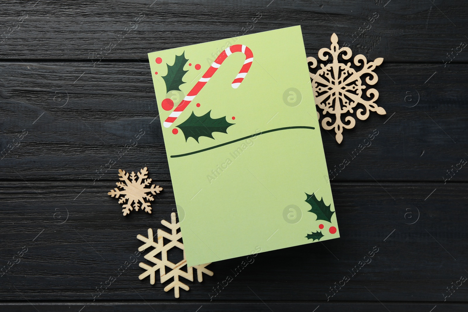 Photo of Blank Christmas invitation card and decorative snowflakes on black wooden table, flat lay