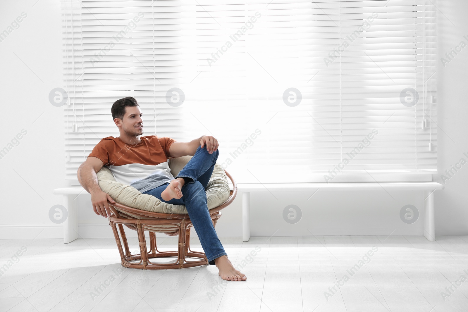 Photo of Attractive man relaxing in papasan chair near window at home. Space for text