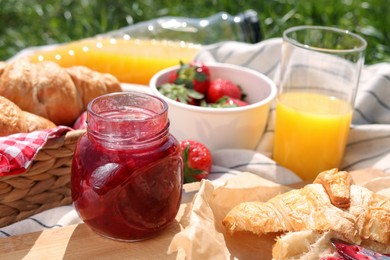 Photo of Jar of jam, juice and croissants on blanket outdoors. Summer picnic