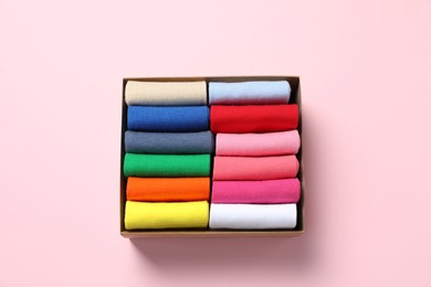 Photo of Box with different colorful socks on light pink background, top view