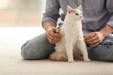 Photo of Young man with cute cat sitting on floor at home