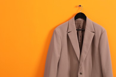 Photo of Hanger with stylish jacket on orange wall, space for text