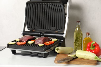 Photo of Electric grill and different products on white wooden table