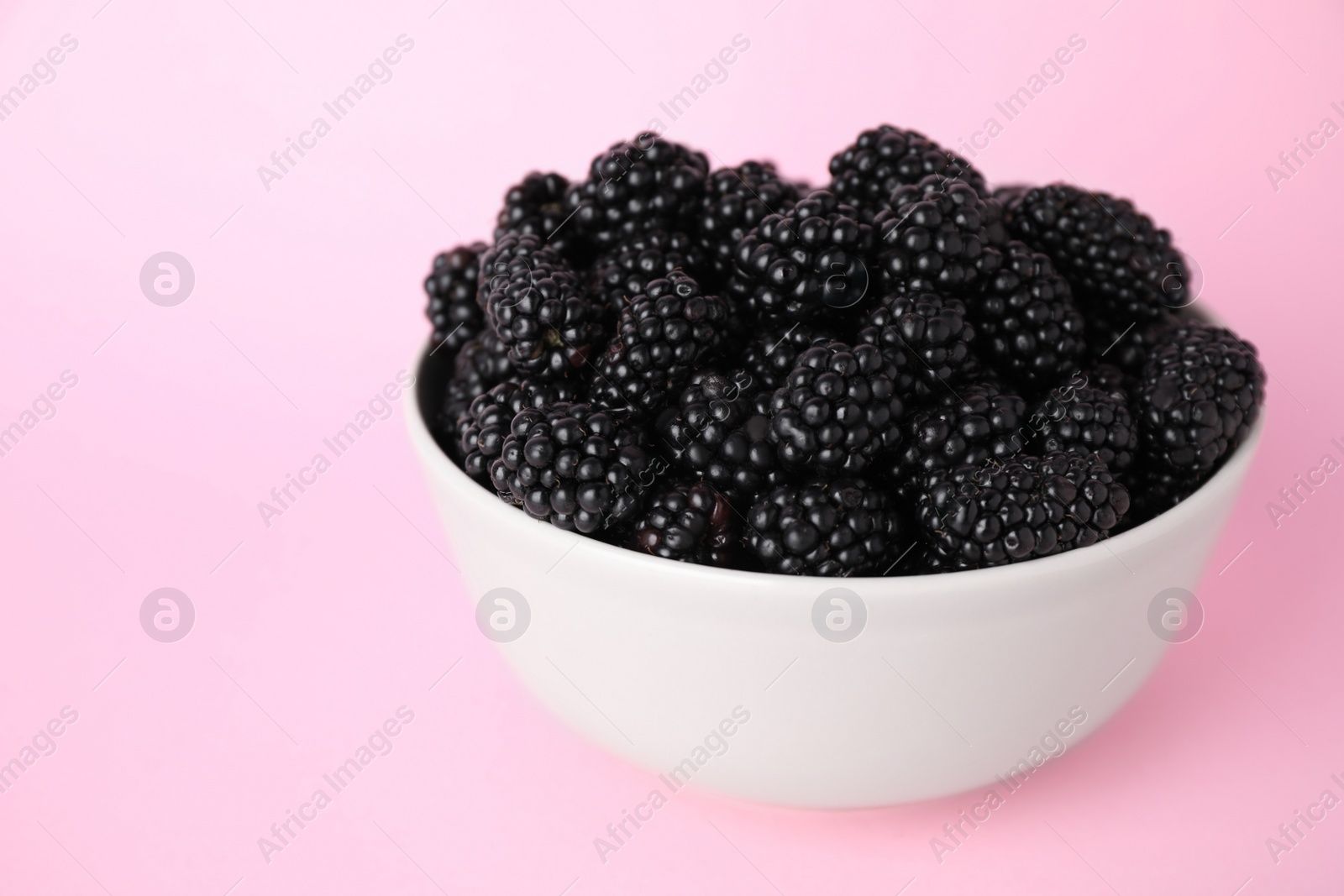 Photo of Fresh ripe blackberries in bowl on pink background
