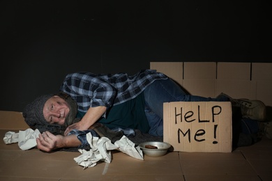 Photo of Poor senior man lying near cardboard sign HELP ME on floor