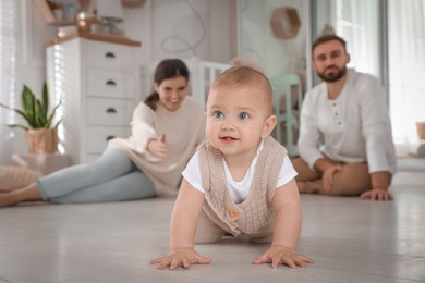 Photo of Happy parents watching their baby crawl on floor at home