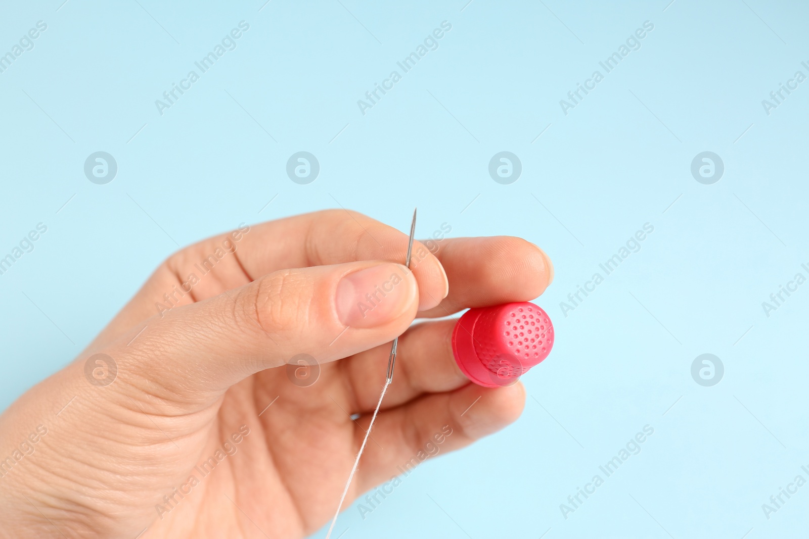 Photo of Woman with thimble, thread and sewing needle on light blue background, closeup