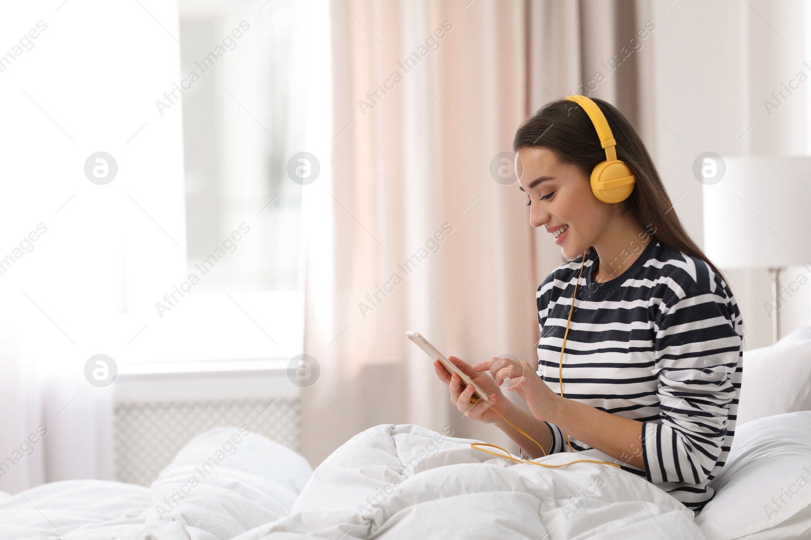 Photo of Young woman with headphones and mobile device enjoying music in bed