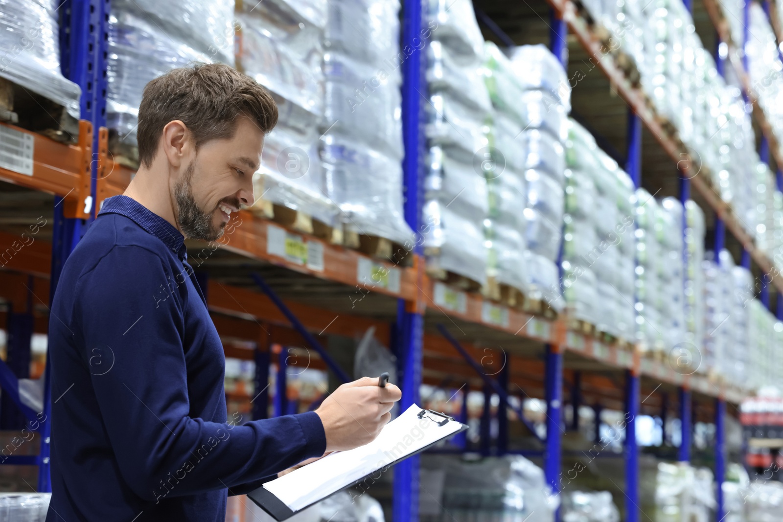 Photo of Happy manager holding clipboard in warehouse with lots of products. Space for text