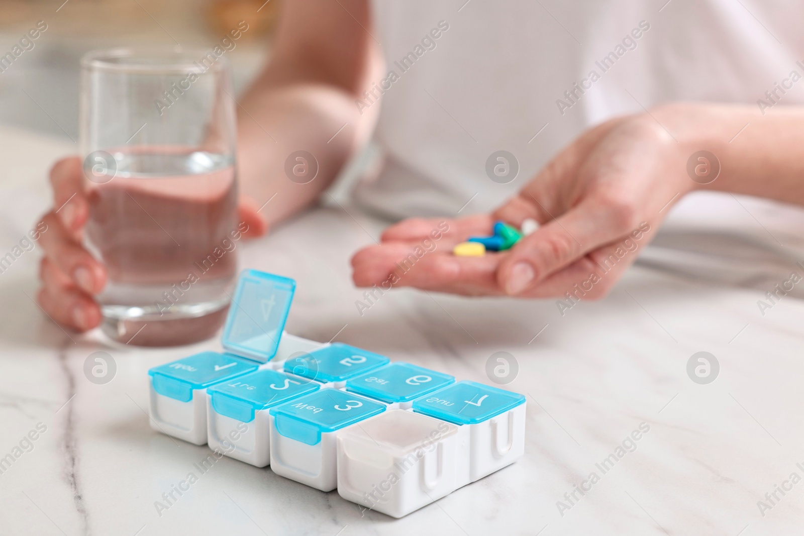 Photo of Woman with pills, organizer and glass of water at white marble table, selective focus