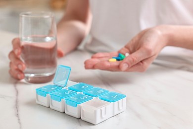 Woman with pills, organizer and glass of water at white marble table, selective focus