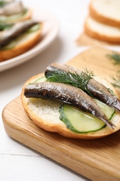 Photo of Delicious sandwich with sprats, cucumbers and dill on wooden board, closeup