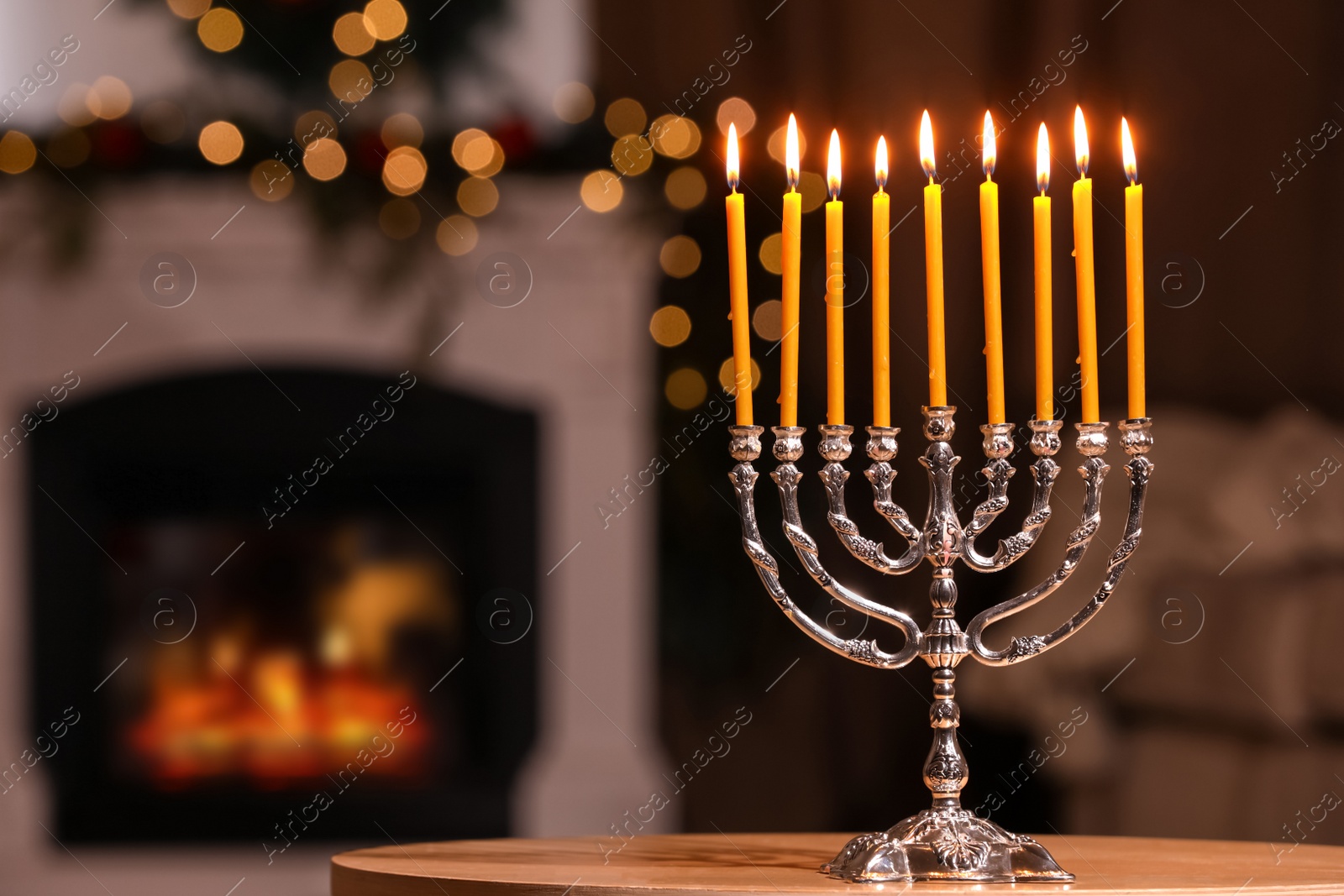Photo of Silver menorah in room with fireplace, space for text. Hanukkah symbol