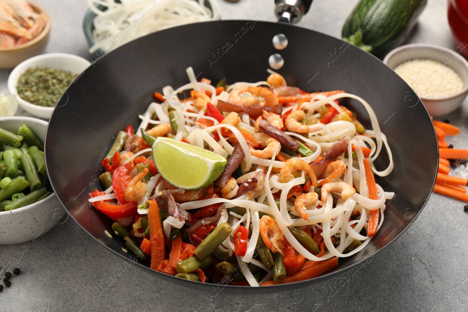 Photo of Shrimp stir fry with noodles and vegetables in wok on grey table