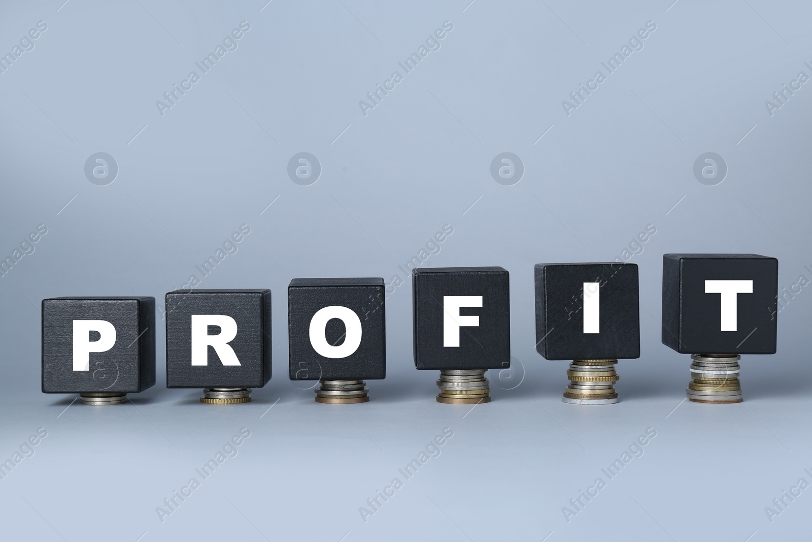Photo of Black wooden cubes with word Profit on stacked coins against light grey background