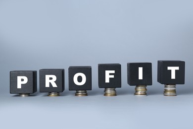 Photo of Black wooden cubes with word Profit on stacked coins against light grey background