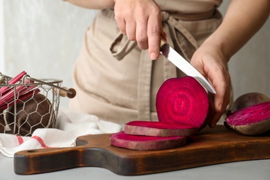 Photo of Woman cutting fresh red beet at table, closeup