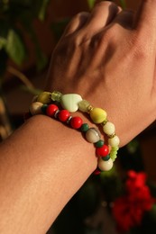 Photo of Woman wearing beautiful bracelets with gemstones on blurred background, closeup