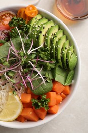 Photo of Delicious vegan bowl with avocados, carrots and microgreens on light grey table, flat lay