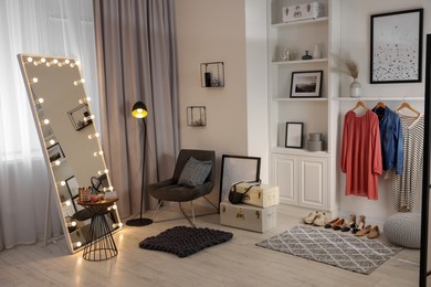 Photo of Makeup room. Stylish mirror with light bulbs, clothes and shoes indoors