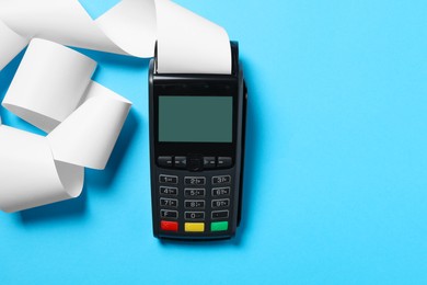 Photo of Payment terminal with thermal paper for receipt on light blue background, top view. Space for text